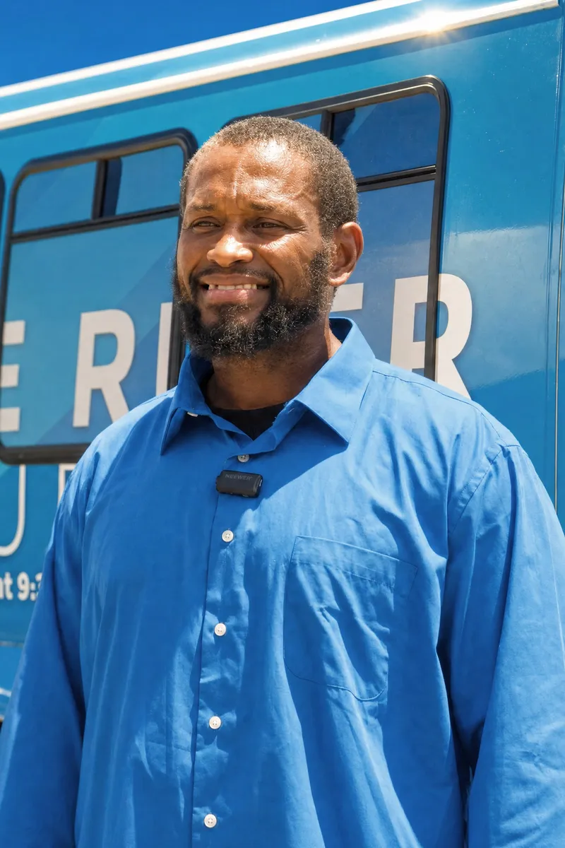 A smiling rider standing in front of a River Church bus